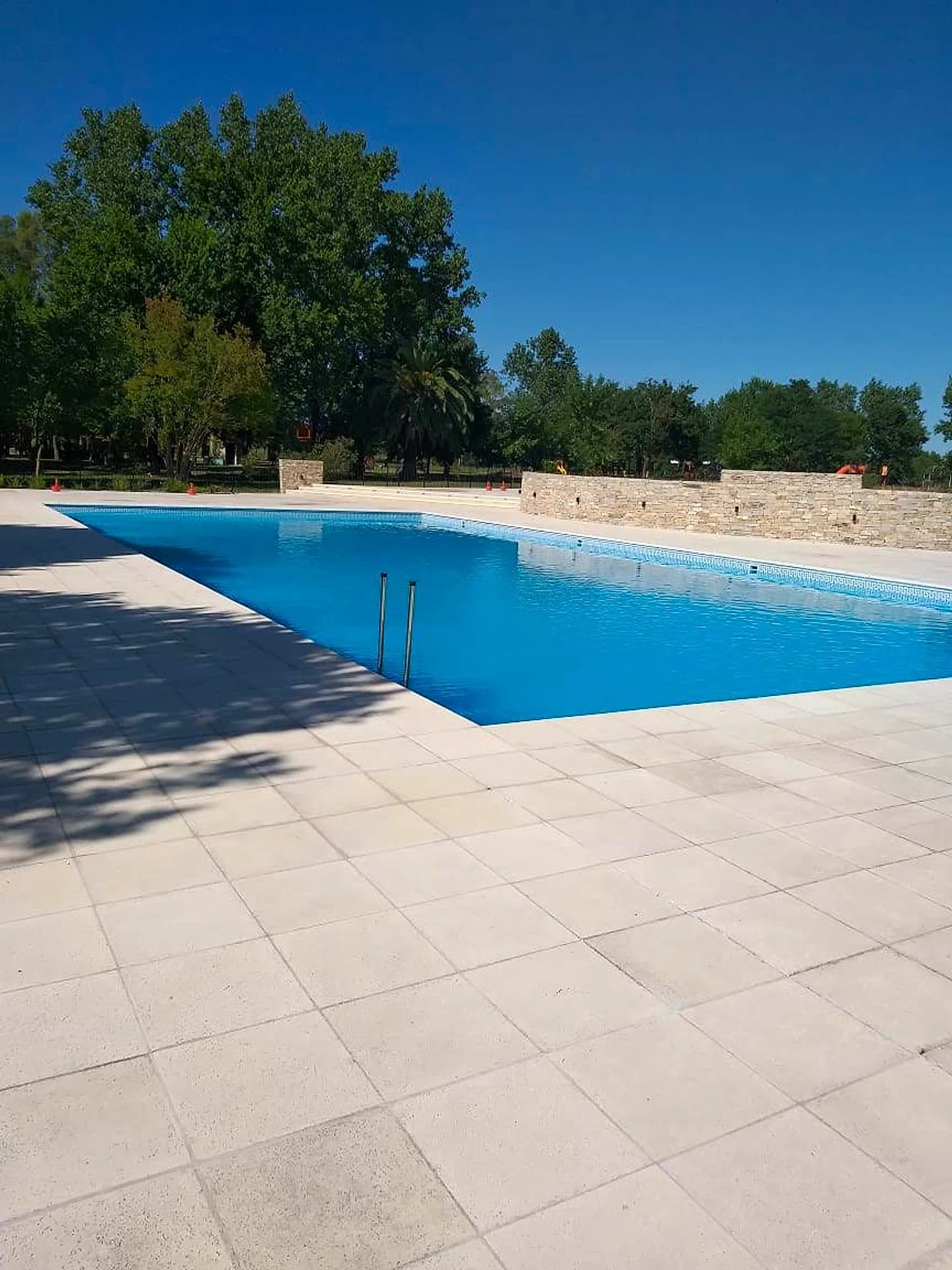 Piscina comercial de gran porte con amplio solárium y muro de piedra